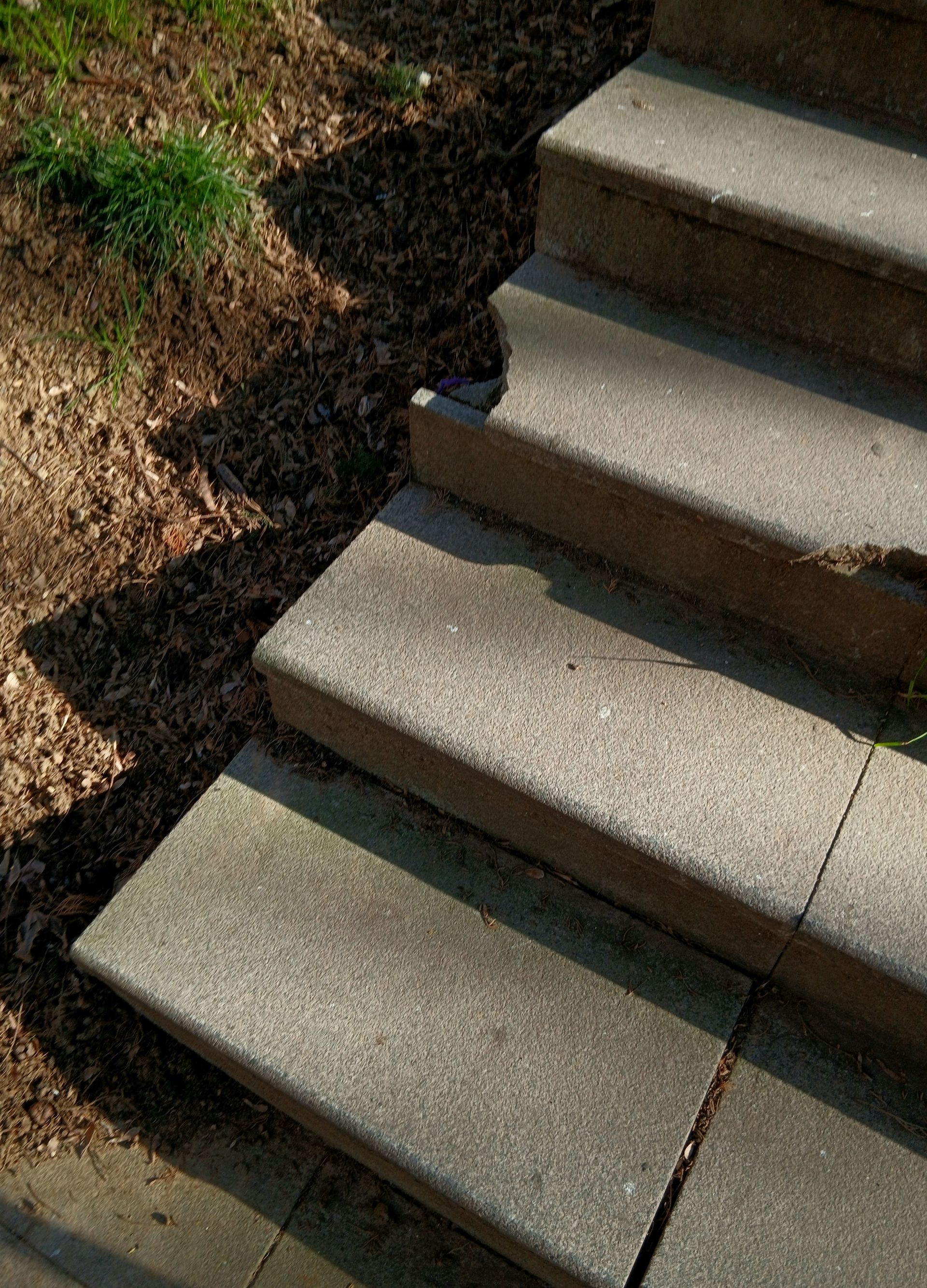 Concrete steps leading outdoors with natural shadows and sunlight.